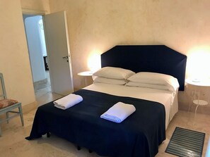 A hotel room with a bed, two bedside tables, a chair, and a door leading to another room.