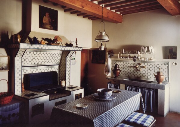 A kitchen with a tiled backsplash, wooden beams, a hanging light fixture, and a stove.