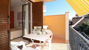 Un balcon avec une table et des chaises, un lit en arrière-plan et un auvent jaune.