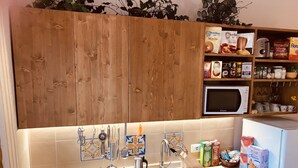Une cuisine avec des meubles de rangement en bois, un four à micro-ondes, un évier orné de carreaux décoratifs et divers ustensiles de cuisine disposés sur le plan de travail.