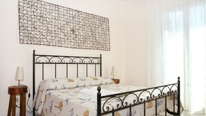 Un lit bien fait, recouvert d’une couvre-lit à motifs, avec une tête de lit décorative en métal et deux tables de chevet dotées de lampes.