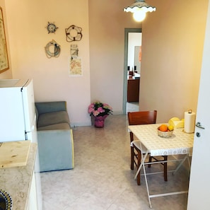 Un espace de vie compact comprenant un coin repas, un canapé, une petite table avec un panier et un réfrigérateur.