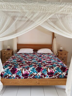 A bed with a floral bedspread, wooden headboard, white pillows, and a canopy. - GROSEILLE PAYS your cottage in Bouillante in Guadeloupe. (BOUILLANTE)
