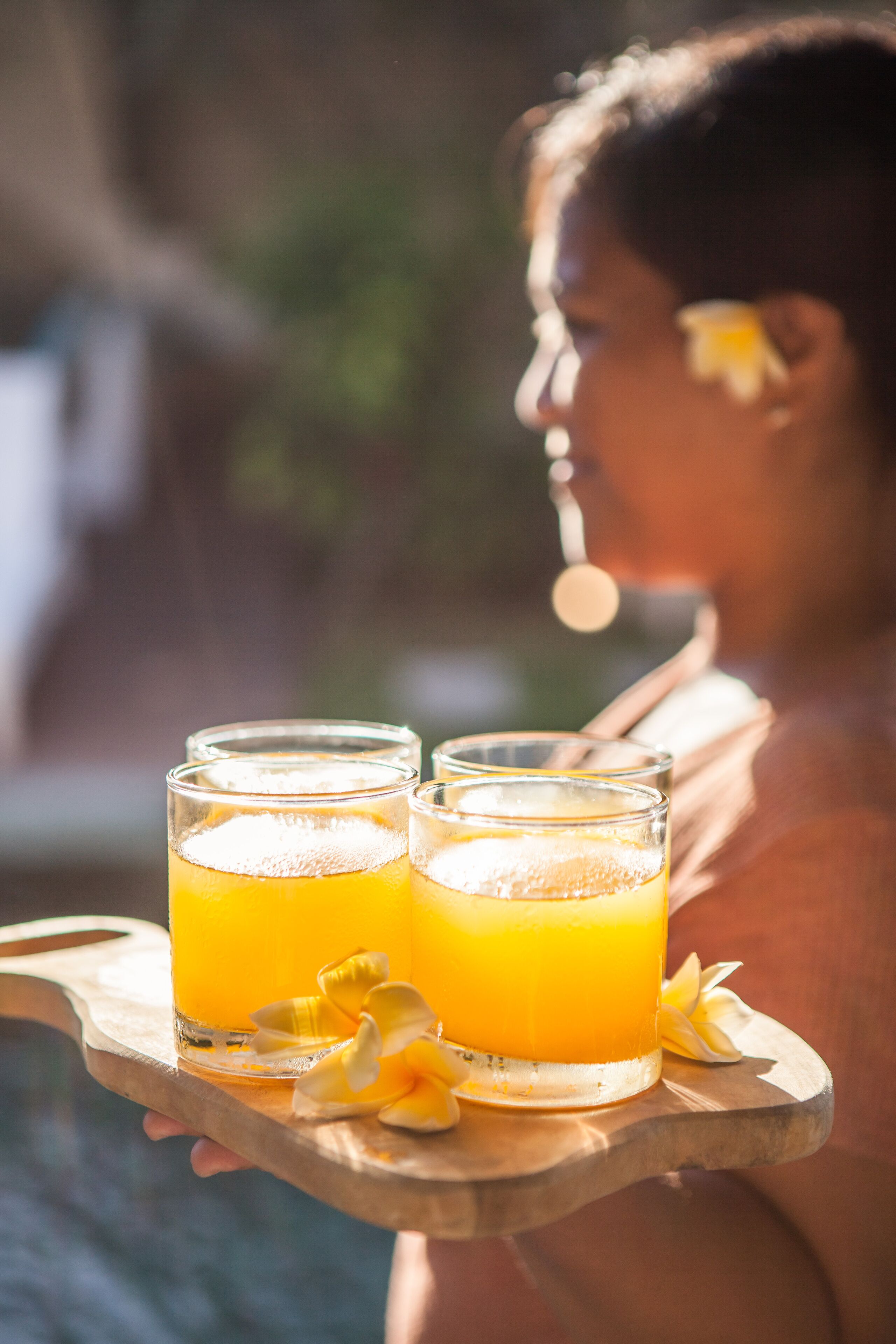 Une personne tenant un plateau sur lequel se trouvent deux verres de jus d’orange et une fleur.