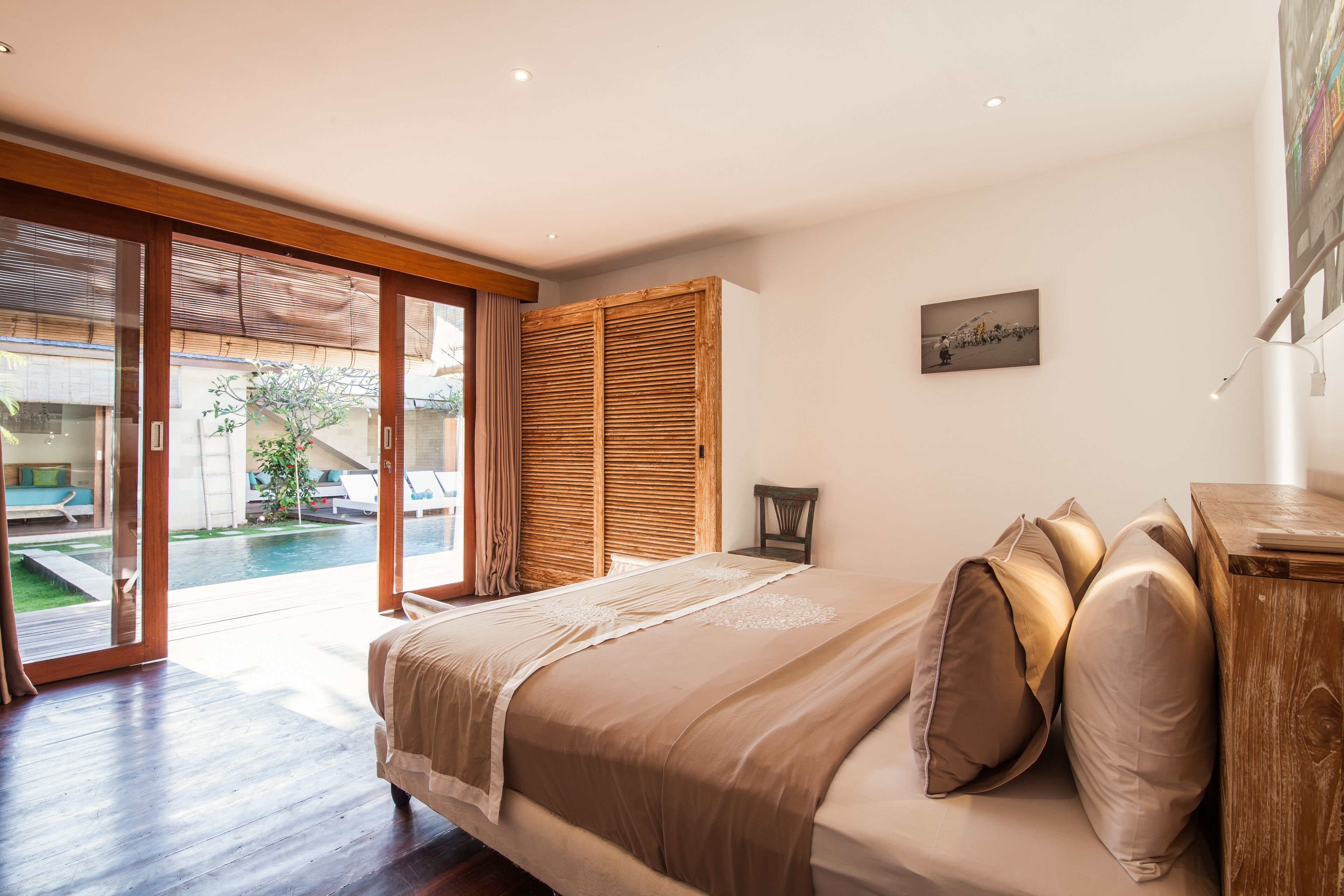 Ein Schlafzimmer mit einem großen Bett, einem Holzkopfteil und Blick auf einen Pool und Außenbereich.