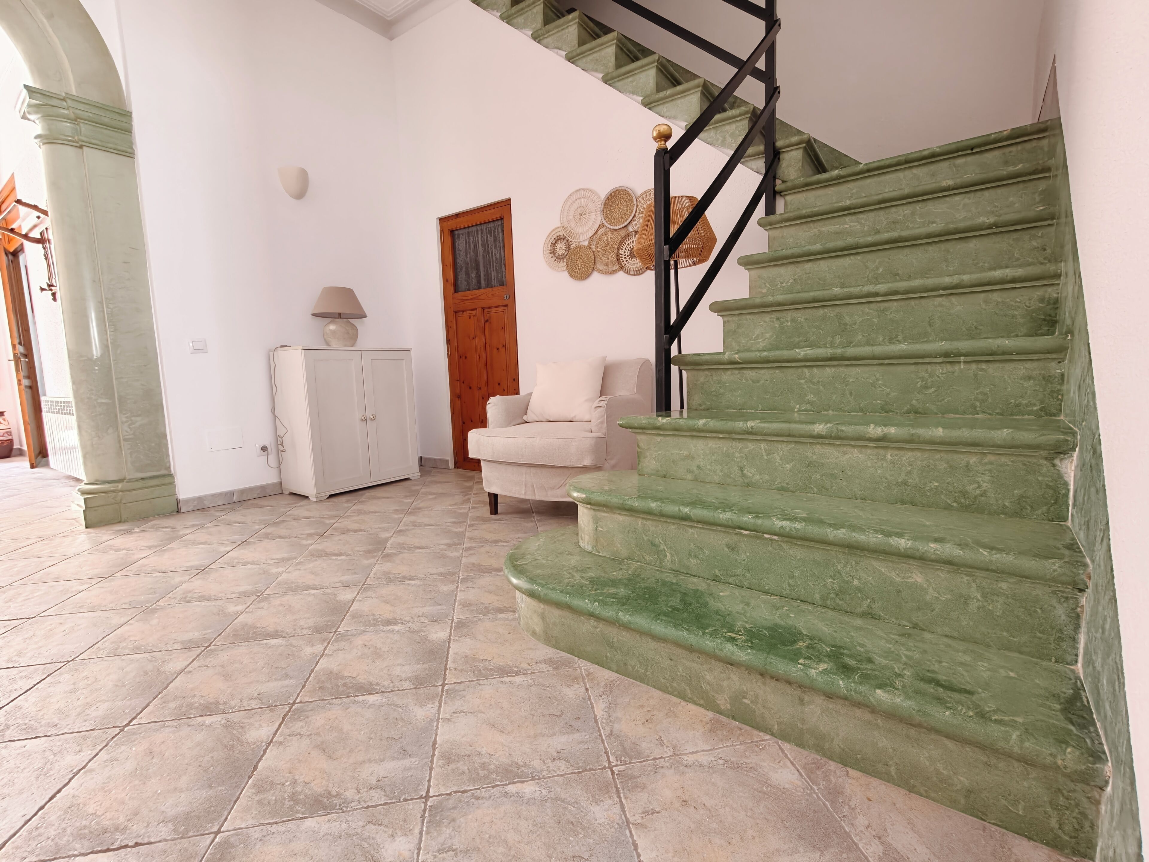 Una escalera con peldaños verdes, un armario blanco, un sofá color beige y una puerta de madera.