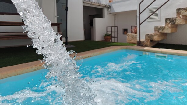 A swimming pool with water cascading into it, a patio umbrella, and a staircase leading to a door.