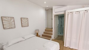 A bedroom with a bed, two wall-mounted artworks, a bedside lamp, a bathroom with a shower, and a staircase.