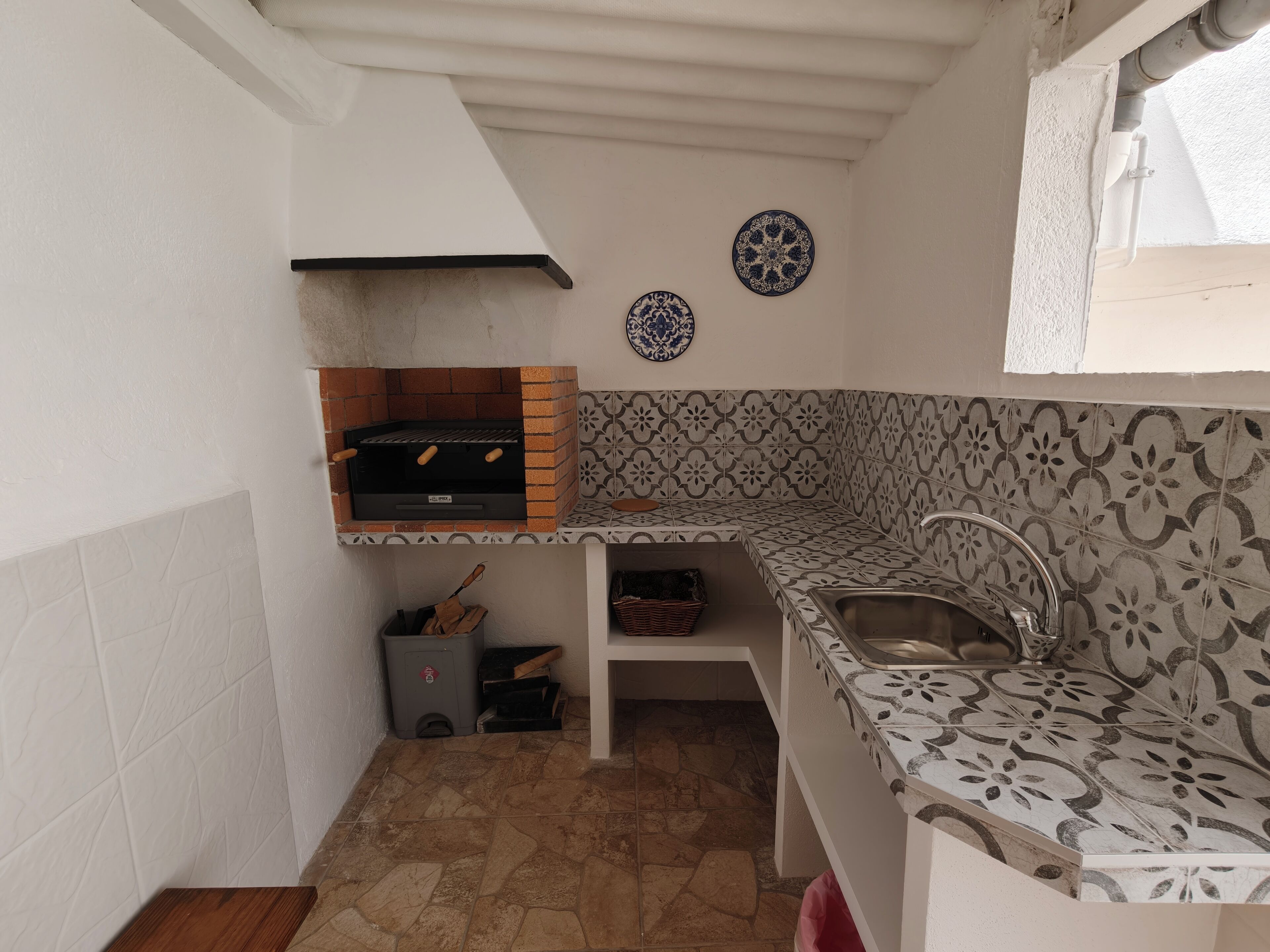 Una cocina compacta con horno integrado, un lavamanos, baldosas estampadas y un plato decorativo en la pared.