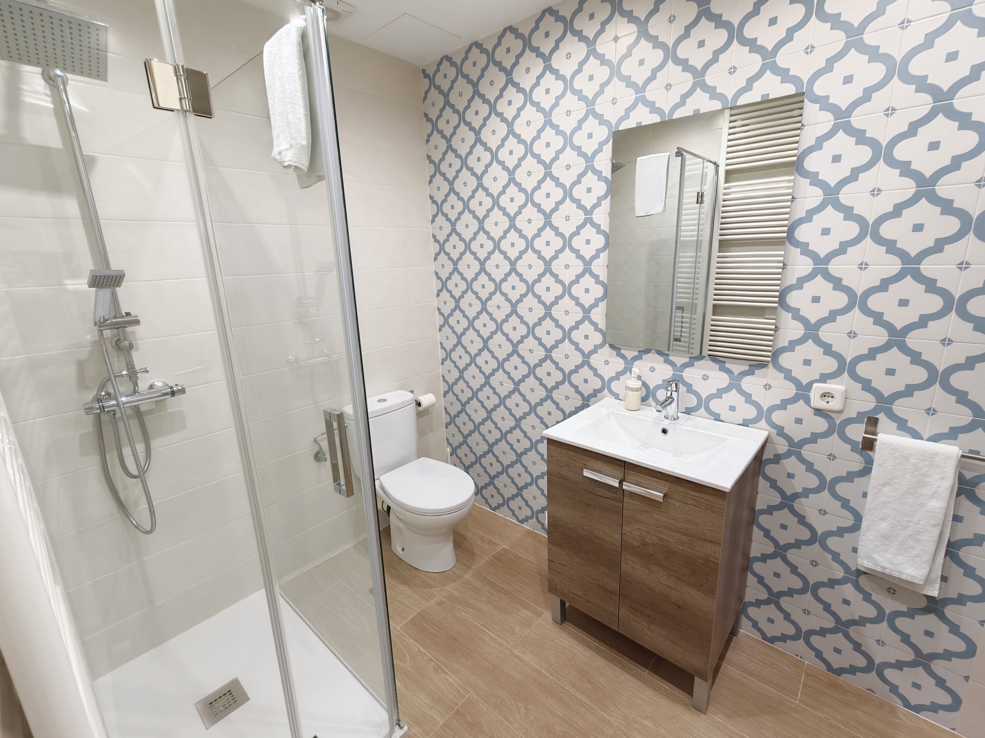 Une salle de bain avec une douche à parois de verre, des toilettes, un lavabo avec un miroir et des carreaux muraux à motifs.