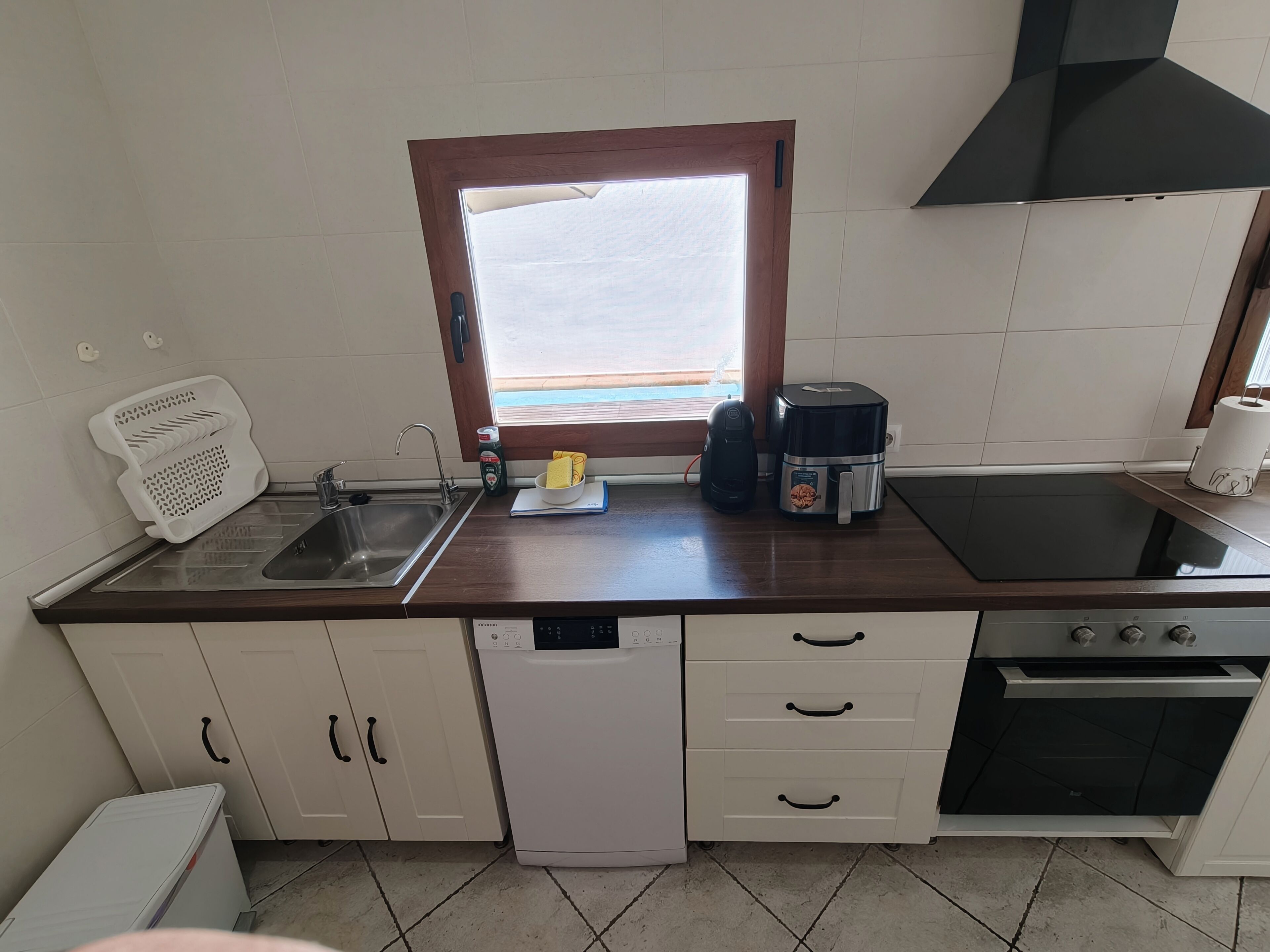 A kitchen with a window, a sink, a dishwasher, a stove, and a countertop with a coffee maker and a rice cooker.
