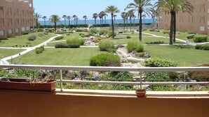 Vue d’une cour d’hôtel agrémentée de palmiers, d’une petite fontaine et offrant une vue dégagée sur l’océan.