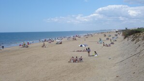 Une vaste plage de sable où l’on peut voir des gens se prélasser au soleil et se baigner.