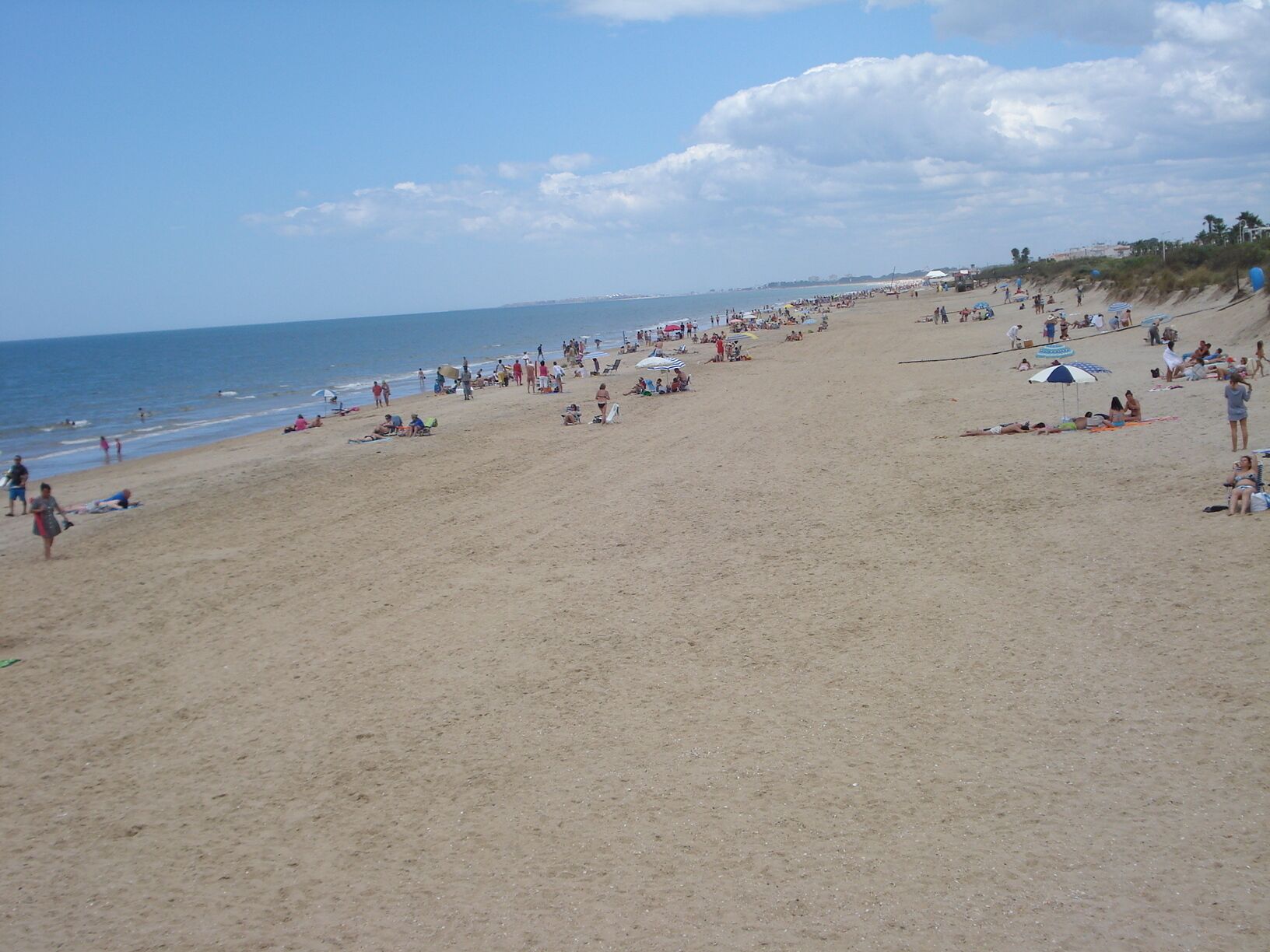 A beach with people sunbathing and walking along the shore.