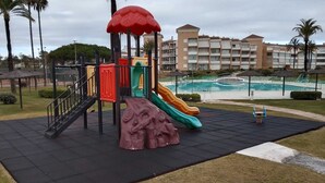Un terrain de jeux avec des toboggans et une structure d’escalade, entouré d’une piscine et de palmiers.