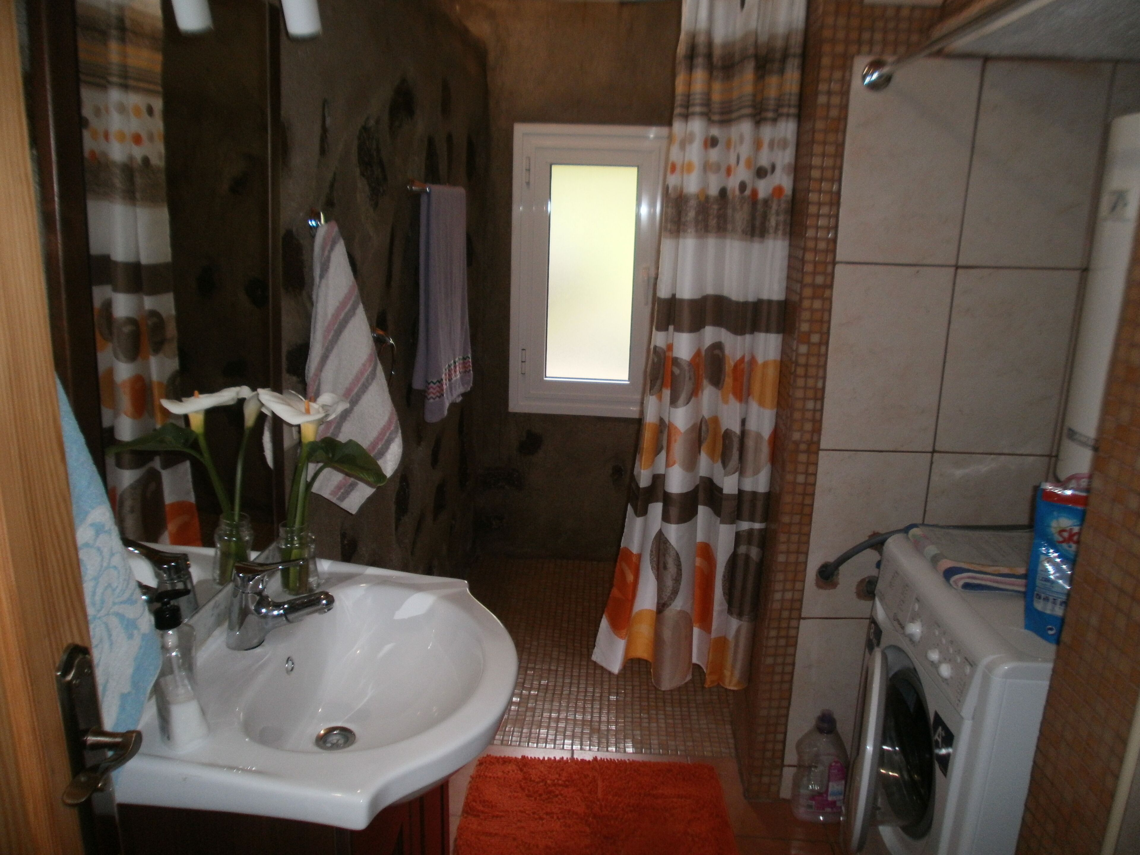 A bathroom with a sink, a window, a washing machine, and a shower curtain.