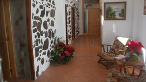 A hallway with a stone wall, wooden door, and a tiled floor leading to a room with a chair and a table. - Traditional Canarian Finca in Las Lajas, Icod de los Vinos, 4 persons (Icod de los Vinos)
