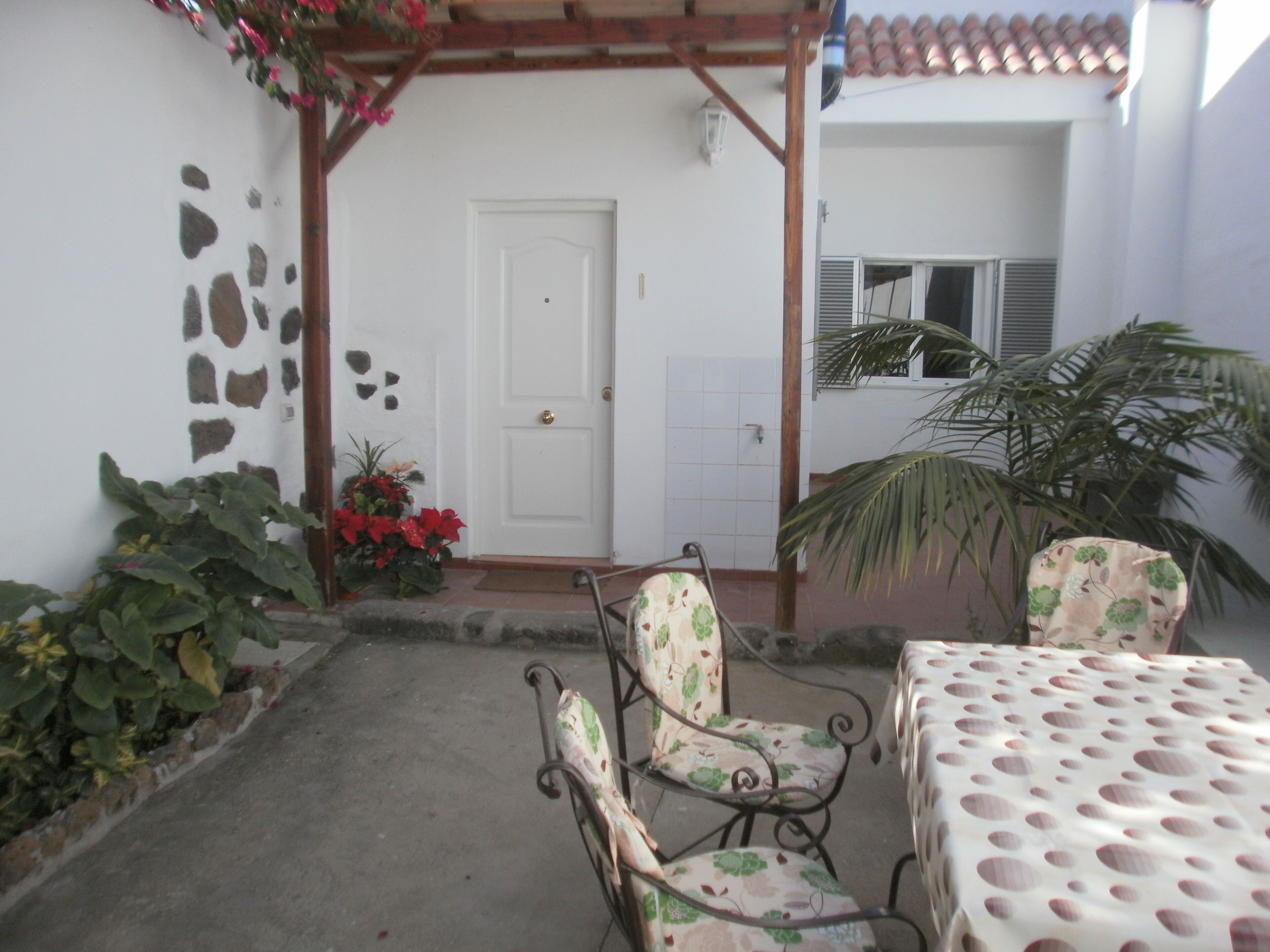A patio with a white door, a table with a polka dot tablecloth, and two chairs with floral upholstery.