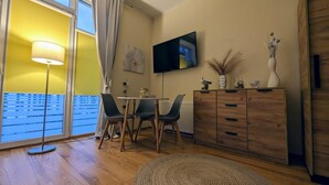 Un salon moderne avec un plancher en bois, une table à manger accompagnée de deux chaises, un téléviseur fixé au mur et un meuble contenant des objets décoratifs.