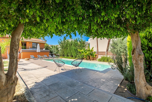 A pool area with lounge chairs, a pool, and a pergola providing shade.