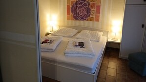 Un letto ben rifatto con lenzuola e cuscini bianchi, due lampade ai lati e un'ampia opera d'arte floreale sulla parete.