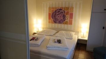 Ein ordentlich gemachtes Bett mit weißen Leinen und Kissen, zwei Nachttischlampen und ein großes Blumenbild an der Wand.