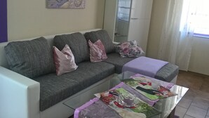 Un soggiorno con un divano grigio, un tavolino in vetro e un quadro appeso al muro.