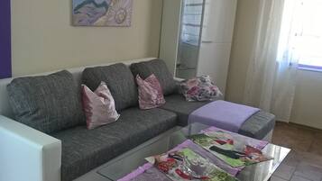 Ein Wohnzimmer mit grauem Sofa, einem Glastisch und einem Gemälde an der Wand.