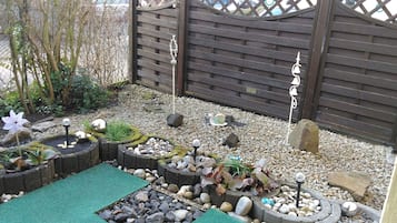 Ein Garten mit Holzlattenzaun, Kies und verschiedenen Pflanzen.