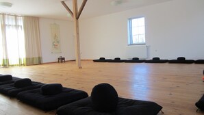 A spacious room with a wooden floor, a large window, and black cushions arranged in rows.