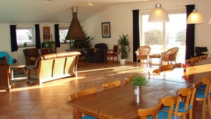 A spacious living room with a wooden dining table, multiple chairs, a sofa, and a large window providing natural light.