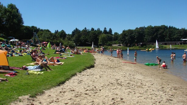 A beach with people sunbathing and swimming.
