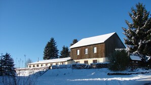 A large wooden building with multiple windows, surrounded by snow-covered trees and a clear blue sky.