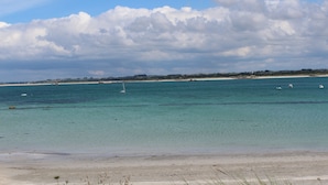 Een strand met helder turquoise water, een zandstrand en een verre kustlijn met gebouwen.