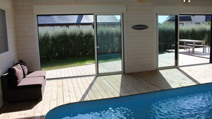 Een zwembadgedeelte met een houten terras, een bank en schuiframen naar buiten.