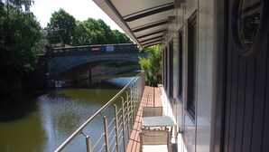 Un balcon avec vue sur une rivière et un pont. On y trouve deux tables et des chaises.