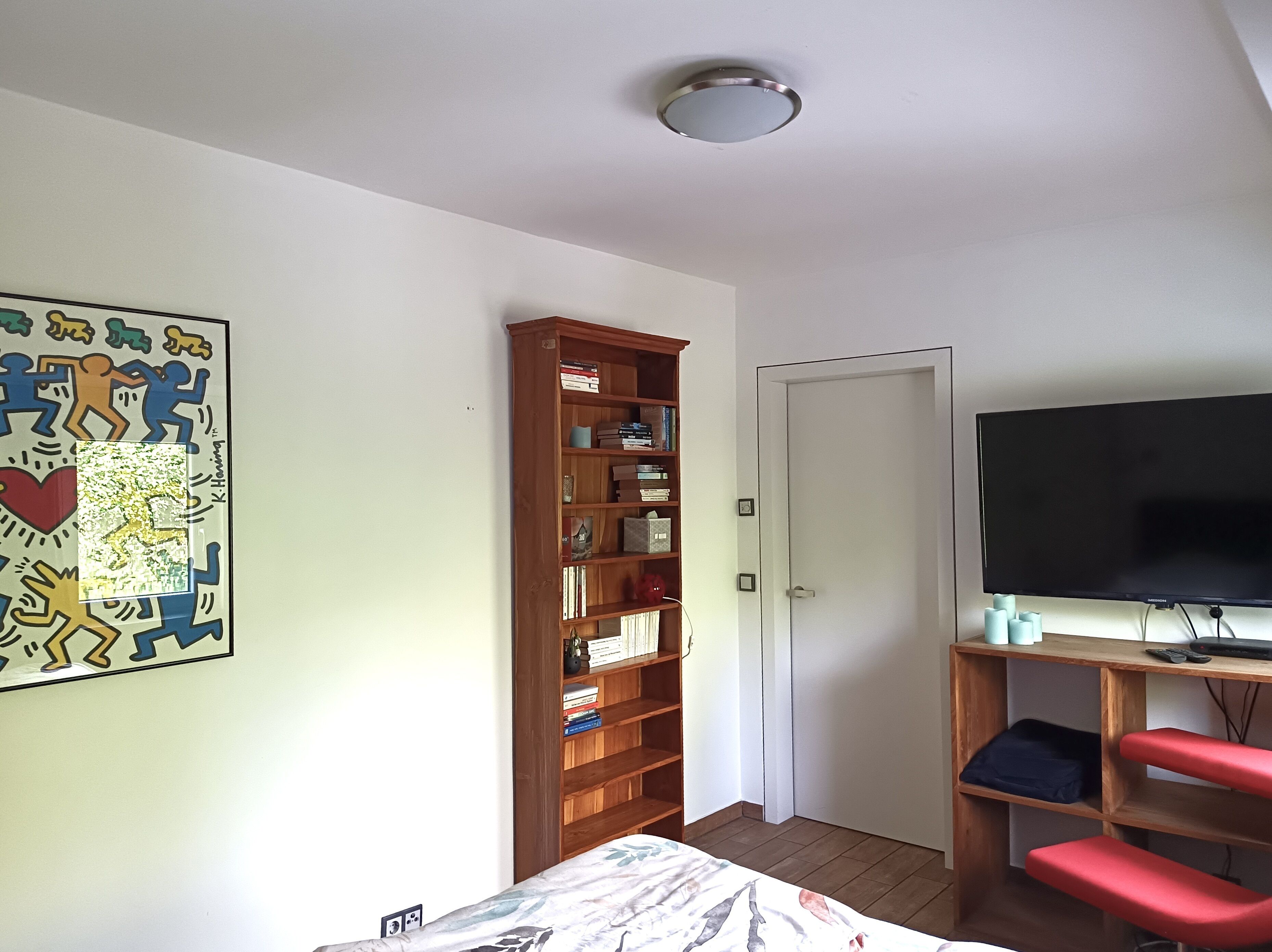 Un dormitorio con cama, una estantería de madera, televisor y una puerta.