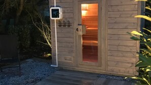 Una cabaña de madera con puerta de vidrio, un porche pequeño y un panel de control en la pared.