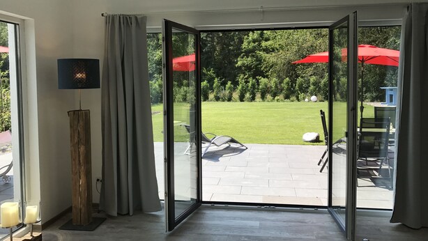 Una habitación con puerta corrediza de vidrio que da a un patio exterior con sombrillas rojas y césped.