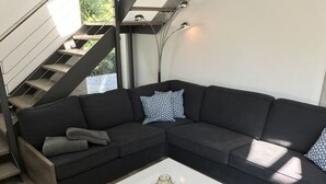 Una sala de estar moderna con un sofá seccional gris oscuro, una mesa de centro blanca y una escalera con barandilla de metal.
