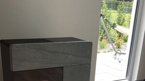 Una chimenea moderna con fuego visible, un tapete negro en el frente y vista a un jardín a través de una puerta de vidrio.