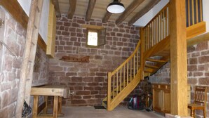 A rustic room with a stone wall, wooden staircase, and a small window.