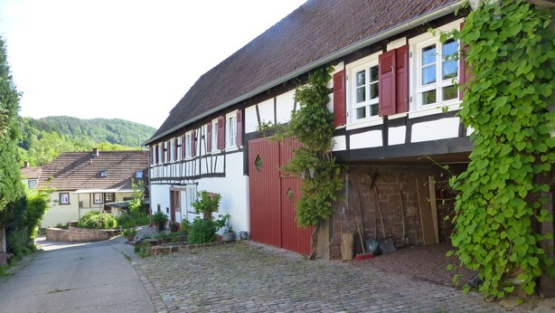 A traditional half-timbered house with a cobblestone driveway and a red barn.