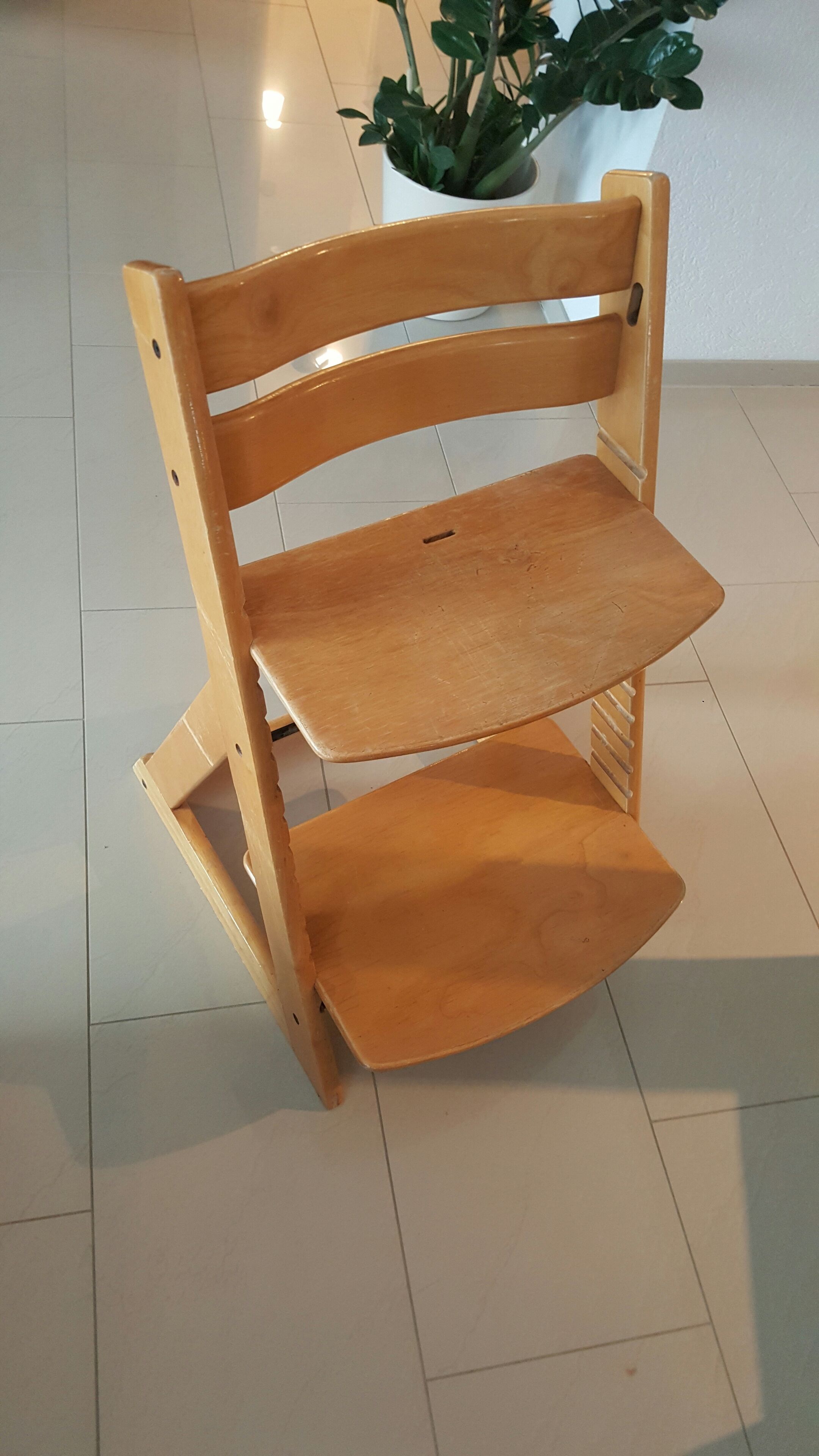 Una silla de madera con respaldo y un estante inferior, sobre un suelo de baldosas.