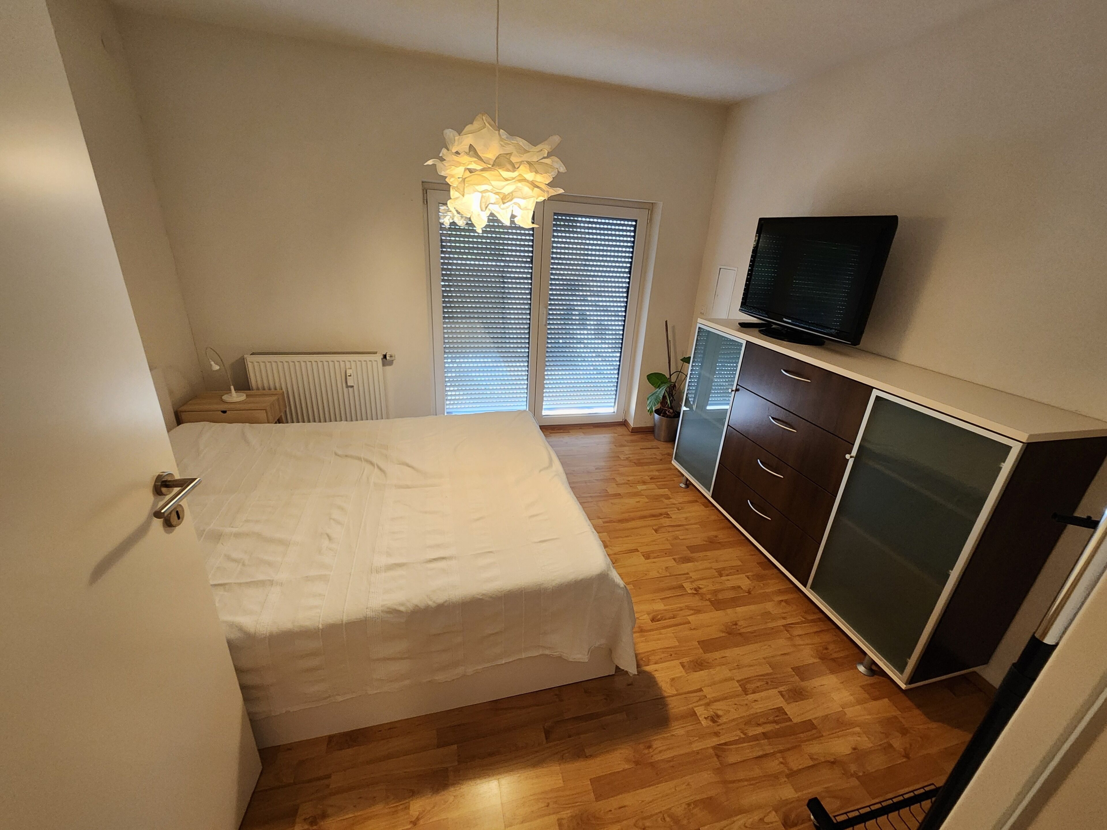 Ein Schlafzimmer mit einem Bett, einem Fernseher auf einem Schrank und einem Fenster mit Jalousien.