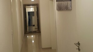 Un couloir avec un plancher ciré, un luminaire au plafond, une porte sur le côté gauche et un tableau encadré sur le mur de droite.