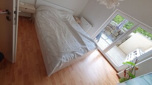 Une chambre à coucher avec un lit, un plancher en bois, une fenêtre donnant sur un espace verdoyant et un luminaire au plafond.