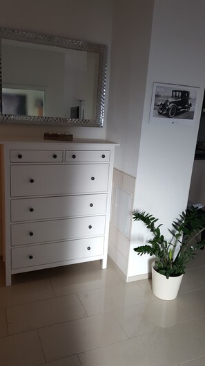 A white dresser with multiple drawers, a mirror above it, and a potted plant beside the wall.