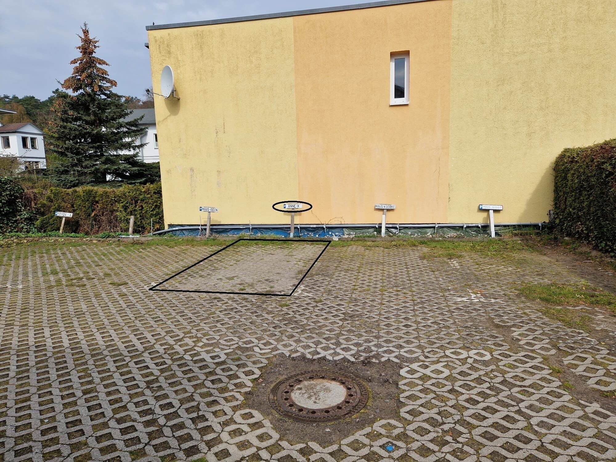 Ein gepflasterter Bereich mit einem Gulideckel, einem gelben Gebäude und Straßenbeschilderung.
