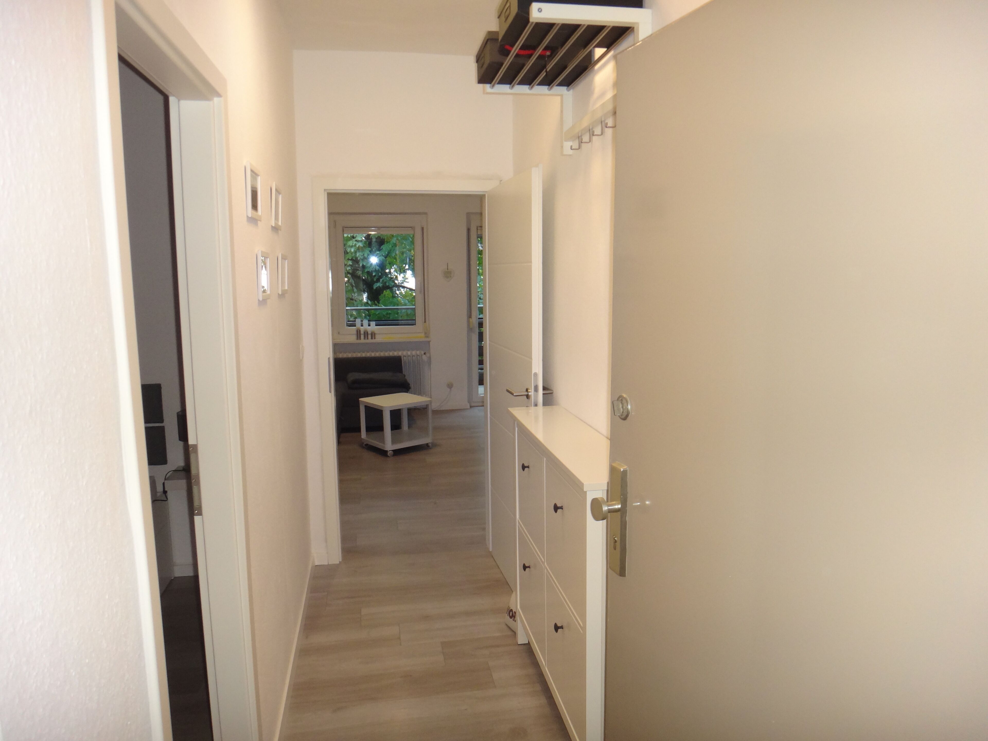A narrow hallway with a wooden floor, a small table, and a bench in the distance.
